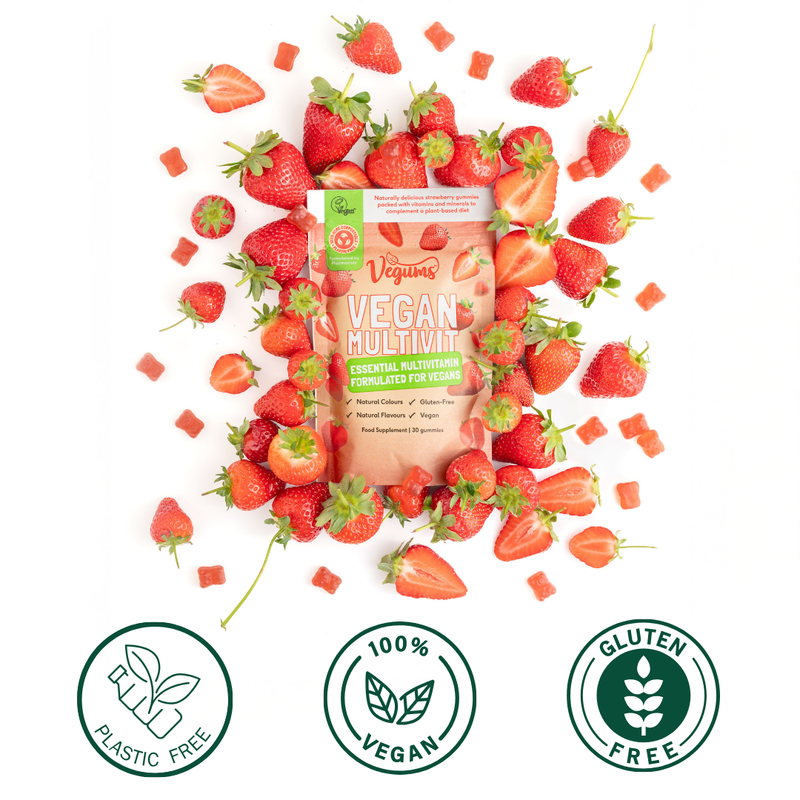 Vegan multivitamin package surrounded by strawberries with '100% Vegan', 'Plastic Free', and 'Gluten Free' labels.