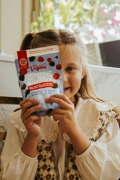 young girl holding a packet of vegums vegan gummy vitamins for kids