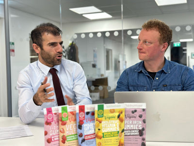two pharmacists talking about vegums vegan vitamins with the packets of vitamins laid out in front of them including vegums iron vitamins 