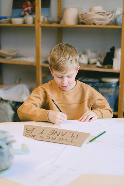 a boy making a sign that talks about the planet and sustainability boy is holdingpencil