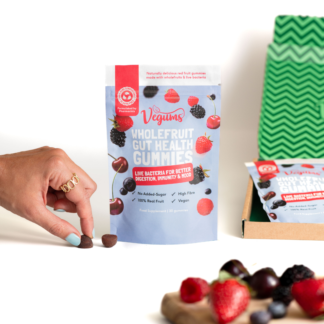Vegums wholefruit gut health gummies packet with fresh fruit laid on a chopping board womans hand holding one of the gummies