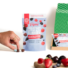 Vegums wholefruit gut health gummies packet with fresh fruit laid on a chopping board womans hand holding one of the gummies