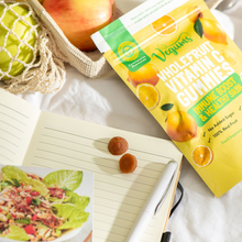 Vegums wholefruit vitamin c vegan gummies packet with two gummies ontop of a notepad with fruit apples in a back on white sheet background