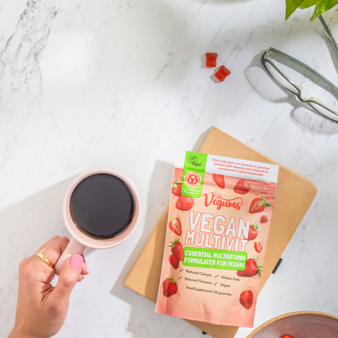 Vegan multivitamin package on a marble surface with a cup of coffee and glasses.