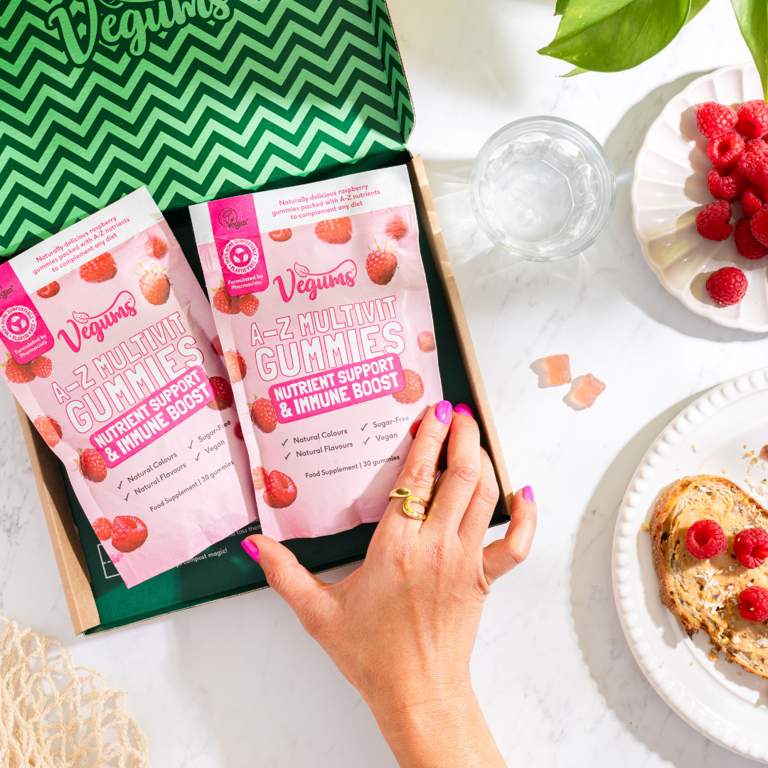 Person holding a box of Vegum's A-Z Multivit Gummies with a plate of raspberries and toast in the background.