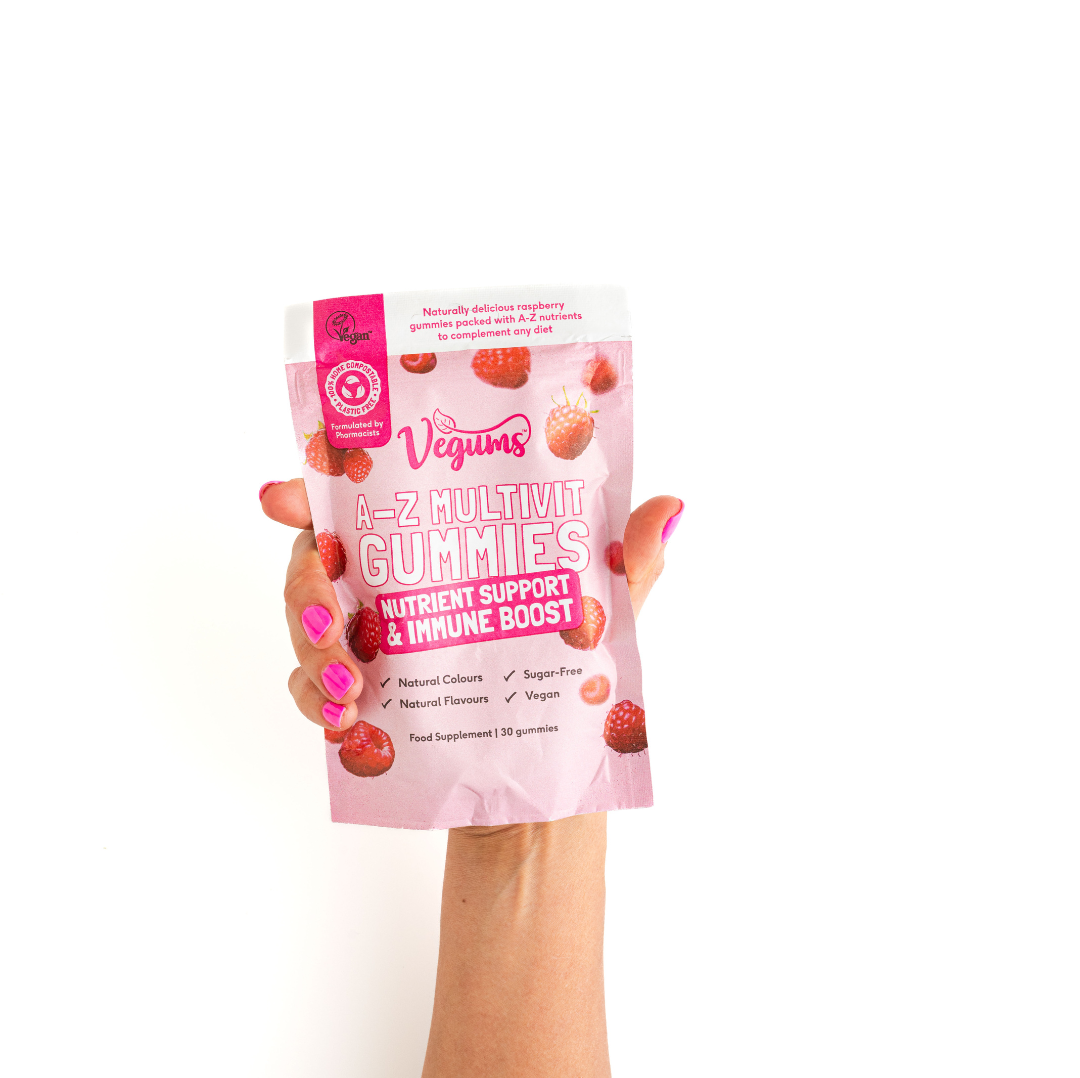Hand holding a pink package of Vegums A-Z Multivit Gummies on a white background