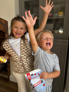Two children in a kitchen with one holding a container of vegums wholefruit gummies.