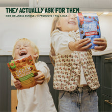 Two children laughing while holding Vegums gummy vitamin pouches in a kitchen