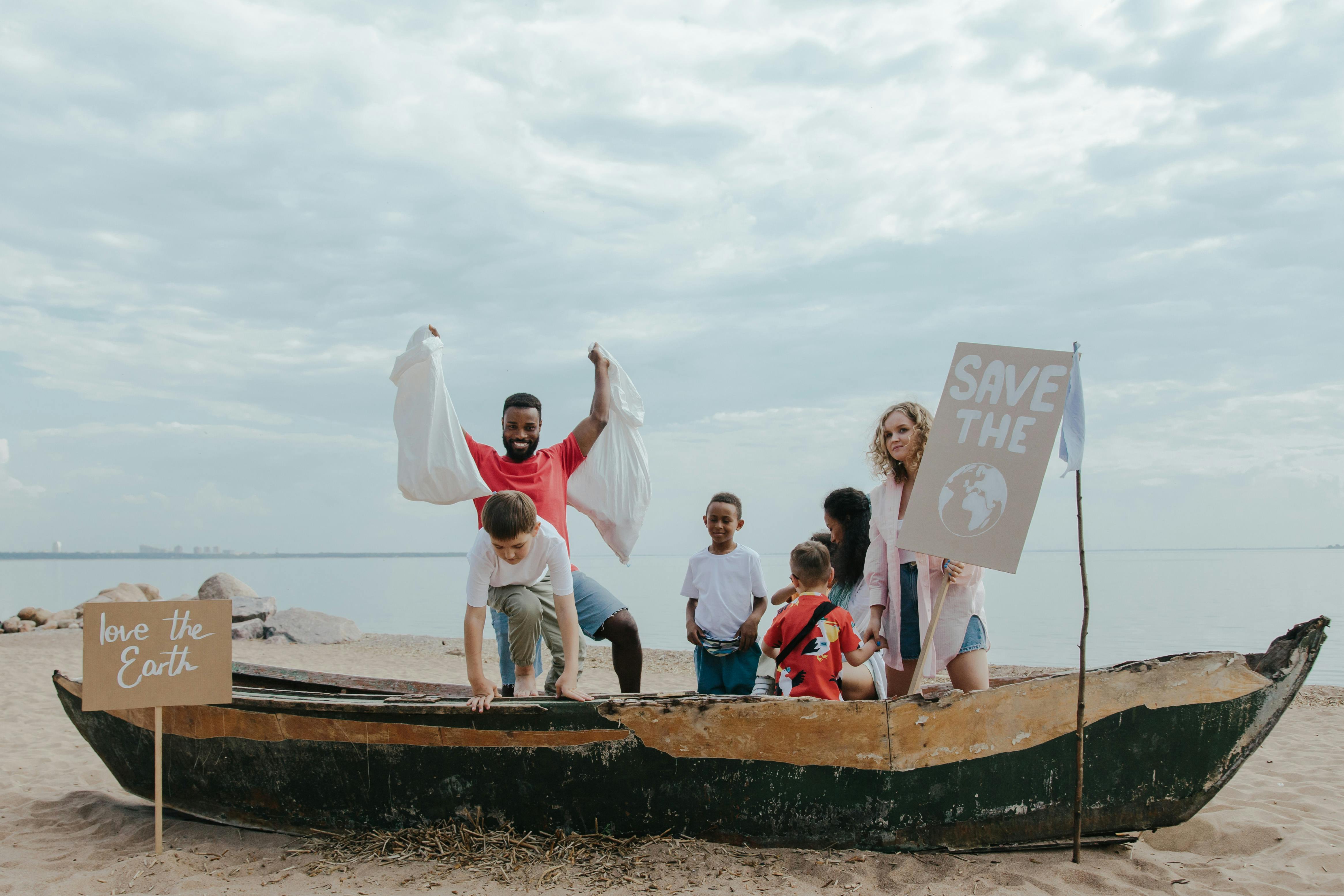 Group of people on a beach with a boat, holding signs about environmental conservation.